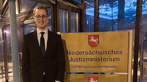 Junger Mann in Anzug steht vor dem Eingang des Landesjustizprüfungsamt (LJPA) in Celle.
